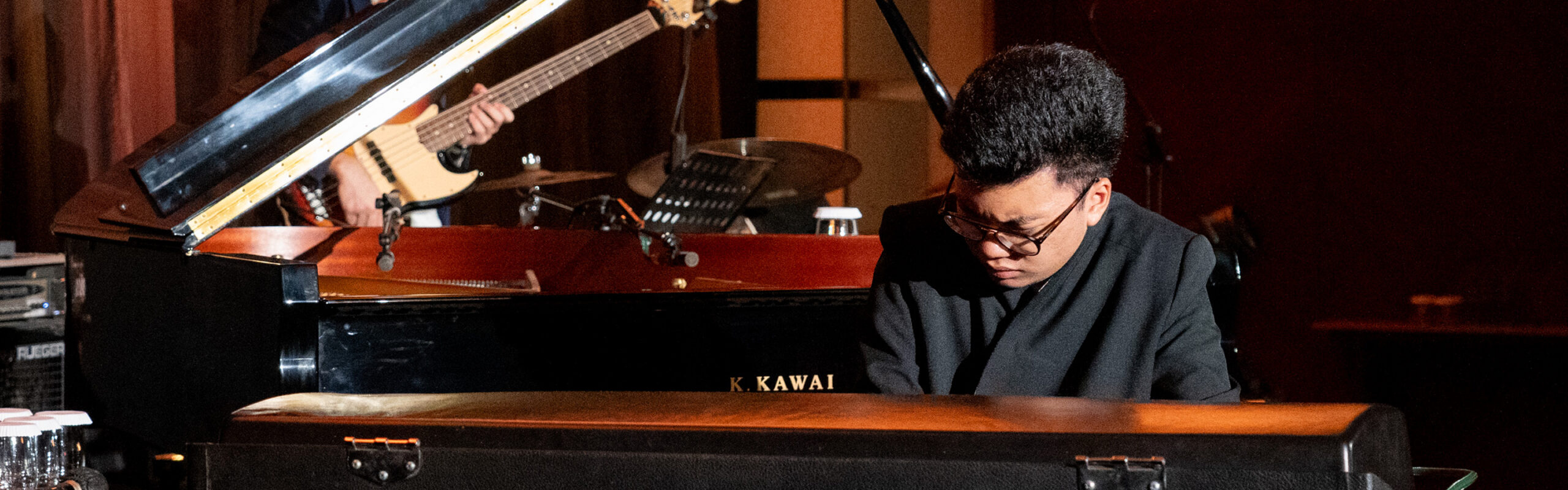 Joey Alexander playing a Kawai grand piano on stage with a bassist behind him