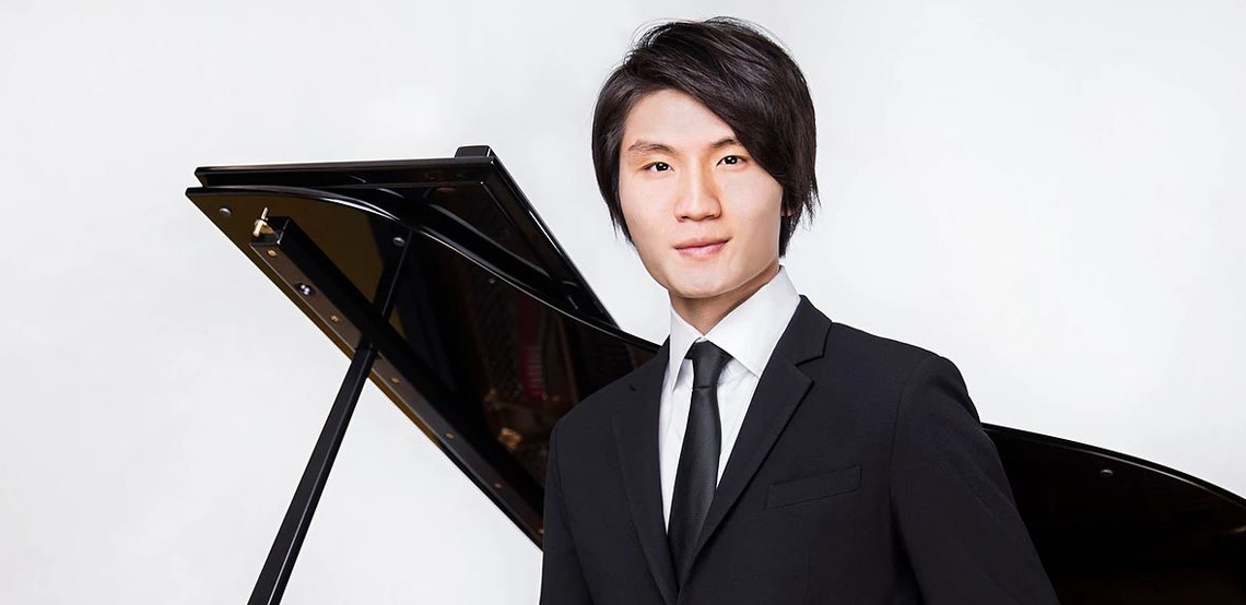 Pianist Niu Niu in a black suit beside an open grand piano in a studio portrait